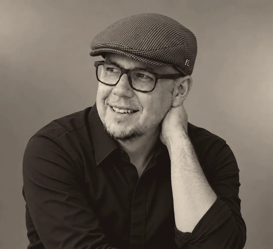 Stefan, Nachschein Studios, mit Schiebermütze und Brille, lächelnd zur Seite blickend